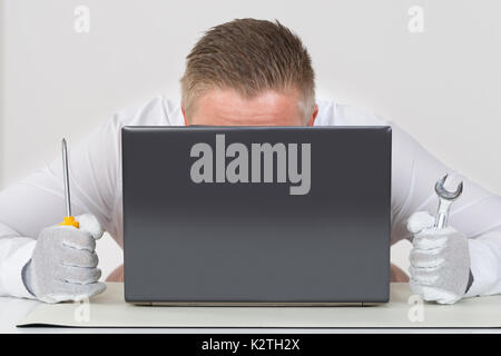 Young Male Technician Holding Screwdriver And Wrench With Laptop Stock Photo