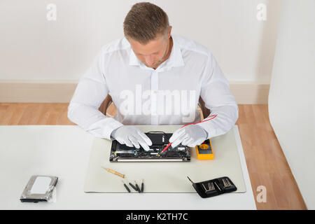 Young Man Examining Laptop Motherboard With Multimeter At Desk Stock Photo