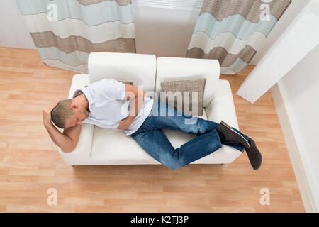 Young Man On Sofa Suffering From Stomach Pain Stock Photo