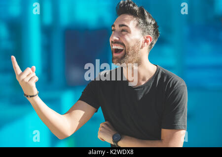 Portrait of young happy man pointing up laughing Stock Photo