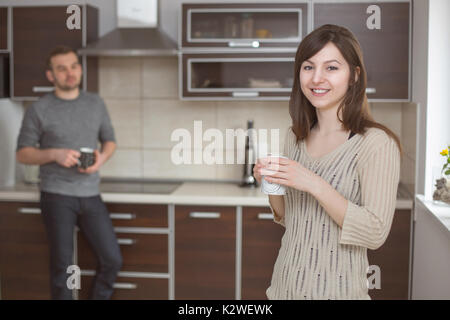 Smiling woman in kitchen with blurred man Stock Photo