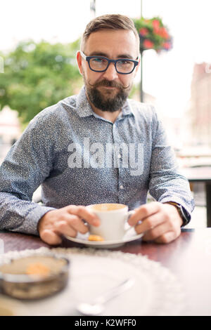 Bearded man sitting in cafe-garden and having cappuccino Stock Photo
