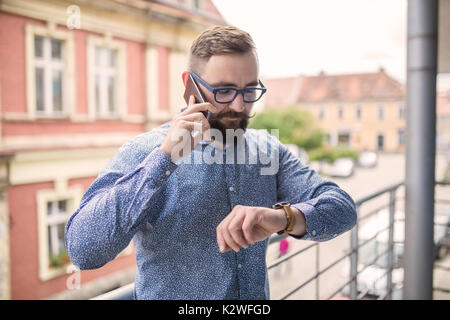 Man standing at balcony, looking at hand watch and calling Stock Photo