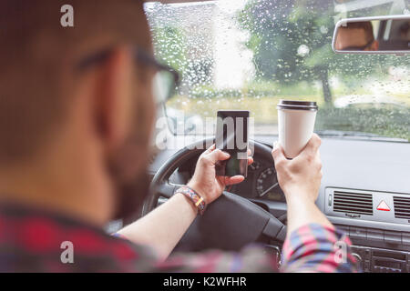 Man using smart phone and having coffee while driving car Stock Photo