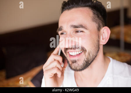 Young latin man having funny phone conversation. He is standing in his bedroom and laughing. Close-up. Stock Photo