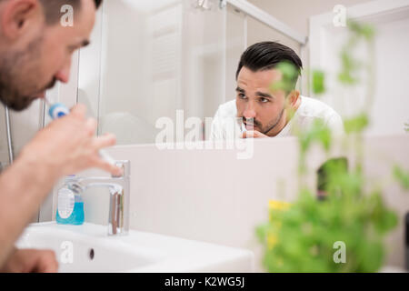 Man brushing his teeth in bathroom. He is looking at himself in the mirror. Stock Photo