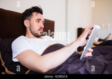 Man surfing the net on tablet in bed Stock Photo
