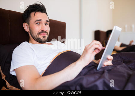 Man surfing the net on tablet in bed Stock Photo