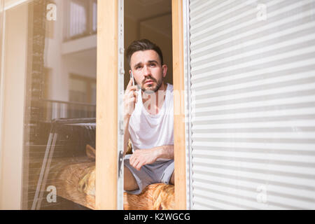 Man talking on the phone in bedroom's window Stock Photo
