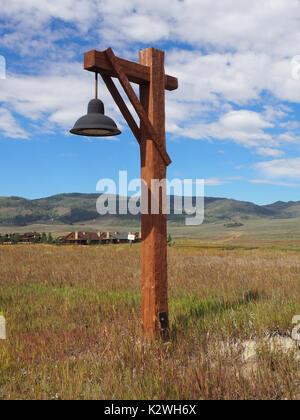 Rustic style wood street light on a prairie in Colorado.  There is a bright blue sky overhead with white puffy clouds.  In the background are mountain Stock Photo