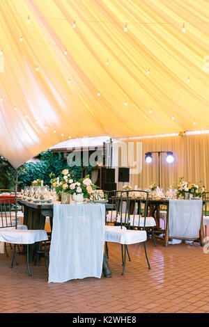 illumination, celebration, happiness concept. restaurant under large yellow like sunset tent prepared for banquet, all the tables are served with dish Stock Photo