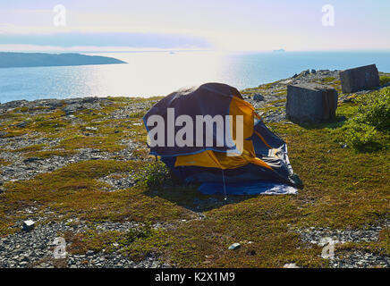 Tent on barren ground high above the Atlantic ocean with icebergs in the mist, St Anthony, Great Northern Peninsula, Newfoundland, Canada Stock Photo
