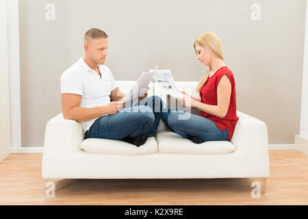 Young Couple Sitting On Sofa Reading Newspapers Stock Photo