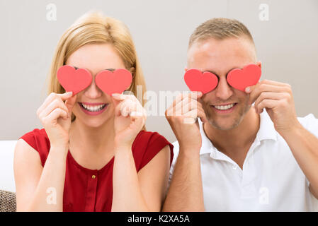 Young Happy Couple Covering Eyes With The Red Hearts Stock Photo