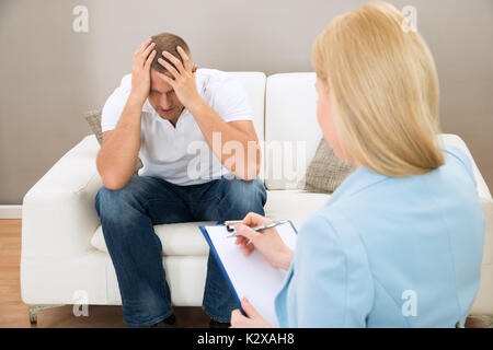 Depressed Patient Sitting On Couch In Front Of Psychiatrist Taking Notes Stock Photo