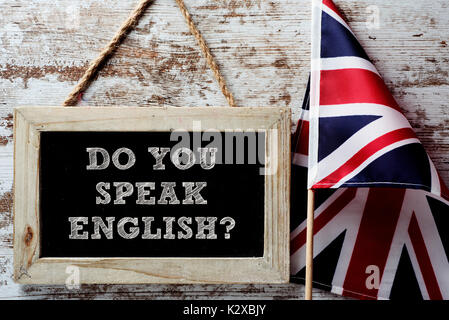 a wooden-framed chalkboard with the question do you speak English? written in it and a flag of the United Kingdom against a rustic wooden background Stock Photo