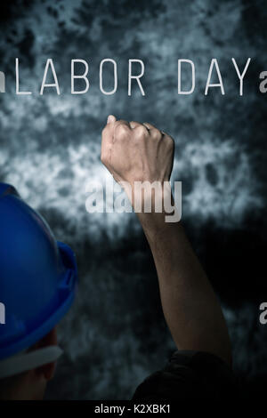 closeup of a young caucasian man seen from behind wearing a blue hard hat and with his fist raised to the air, against a gradient gray background and  Stock Photo