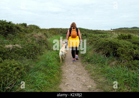 Woman with orange rucksack and dog walking along the Wales Coast Path between St Non's and Porthclais in summer Pembrokeshire UK  KATHY DEWITT