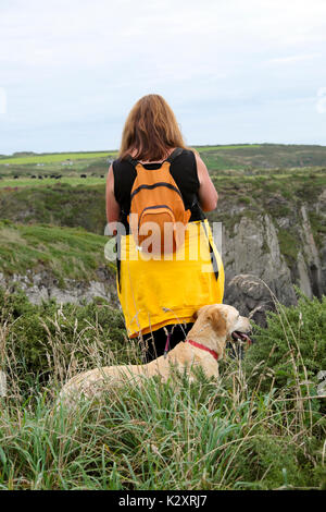 Woman with orange rucksack and dog walking along the Wales Coast Path between St Non's and Porthclais in summer Pembrokeshire UK  KATHY DEWITT Stock Photo