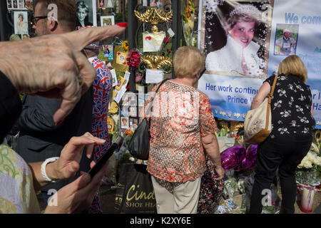 As crowds of royalist well-wishers gather, a spontaneous memorial of flowers, photos and memorabilia grows outside Kensington Palace, the royal residence of Princess Diana who died in a car crash in Paris exactly 20 years ago, on 31st August 2017, in London, England. In 1997 a sea of floral tributes also filled this area of the royal park as well as in the Mall where her funeral passed. Then, as now - a royalists mourned the People's Princess, a titled coined by the then Prime Minister Tony Blair. Stock Photo