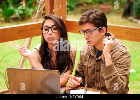 Hipster couple concentrated and working in their computer on porch of wooden house, summer relaxing together concept, in a backyard background Stock Photo
