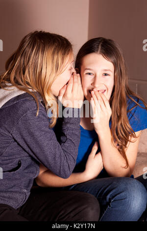 Teenage sisters or girlfriends telling secrets in a whisper. Stock Photo