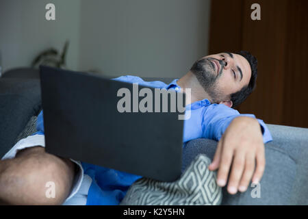 middle aged arab man fallen asleep while working in laptop on a sofa in his city apartment Stock Photo