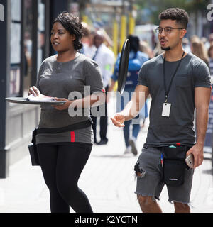 LONDON, ENGLAND - August 20, 2017 Young boy and girl with a tray give out leaflets on the street Carnaby Street Stock Photo