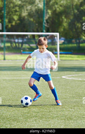 Boy soccer player running with ball on football stadium Stock Photo