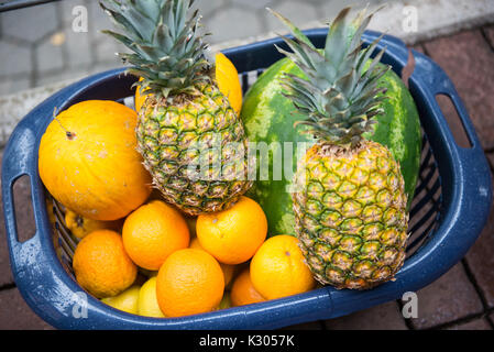 different ripe fruits in a plastic basket on pavement Stock Photo