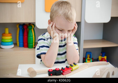 Bored sad little boy sitting at table. sad bored boy child toy activity baby kindergarten concept Stock Photo