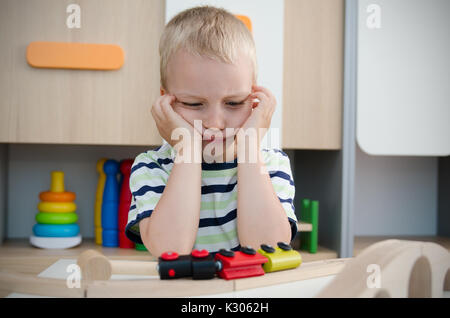 Bored sad little boy sitting at table. sad bored boy child toy activity baby kindergarten concept Stock Photo
