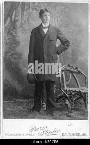 Charles Angelo Conrad, lawyer and graduate of Johns Hopkins University, poses for his portrait in a studio with staged grass and chair made of wooden branches, standing in a suit holding his hat, Baltimore, Maryland, 1894. Stock Photo