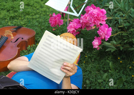 Man lying on grass and writing music ideas on music sheets, outdoor summertime photo Stock Photo