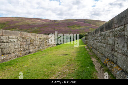 Top of grassy bank of dam at Hopes Reservoir, East Lothian, Scotland, UK, with wall built of stone from old Calton Jail in Edinburgh in 1930s Stock Photo