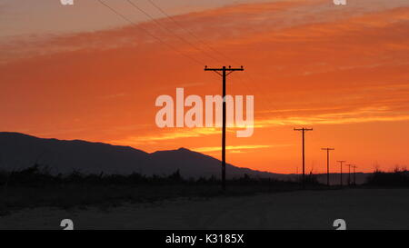 Line of electric power poles transmission lines disappearing into the distance at sunrise in California Anza-Borrego desert Stock Photo