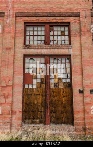 Huge doors in an old, historic building with broken glass and wood making a patchwork design where the windows once were Stock Photo