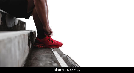 Close-up runner tying shoelace on the steps, isolated on white background with copy space, healthy lifestyle Stock Photo