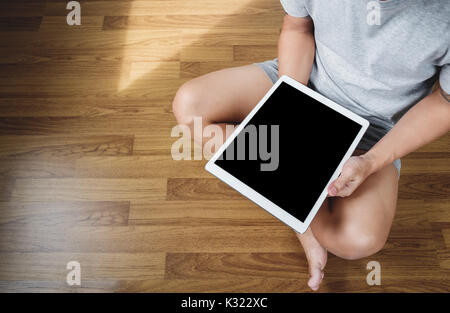 a man using digital tablet computer on wooden floor, in casual clothing, blank empty device screen, above view Stock Photo