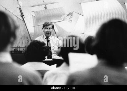 A choir director looking at his music sheets in front of his choir in front of a mural of boats and ships at Johns Hopkins University, Baltimore, Maryland, 1980. Stock Photo