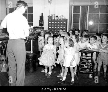Students in the kindergarten class of an elementary demonstration school of Johns Hopkins University stand and watch in fascination while a glass blower works on a piece with his back turned, during a summer field trip to a glass blowing studio, July, 1950. Stock Photo