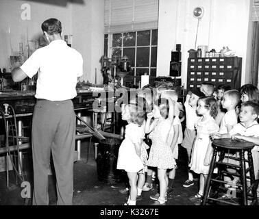 Students in the kindergarten class of an elementary demonstration school of Johns Hopkins University stand and watch in fascination while a glass blower works on a piece with his back turned, during a summer field trip to a glass blowing studio, July, 1950. Stock Photo