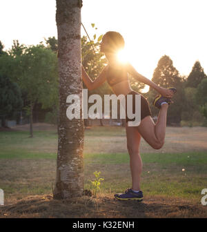 A female runner stretches her legs at sunset in a park. Stock Photo