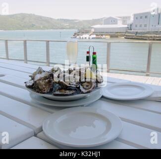 a plate of fresh open oysters and a glass of champagne on a white table with a view of the ocean, South Africa, selective focus Stock Photo