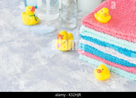 stack of towels with yellow rubber bath ducks and means for bathroom on white marble background, space for text, selective focus Stock Photo