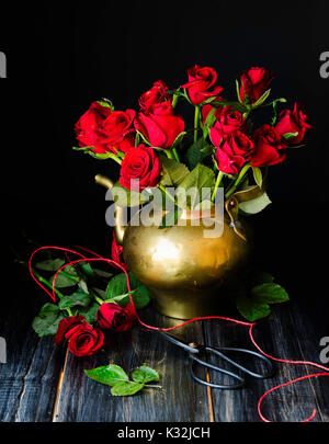 Bouquet of red roses in a copper jar with scissors on a black background, selective focus, concept Stock Photo