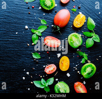 colored slices of tomato with basil and spices on black stone background selective focus, space for text Stock Photo