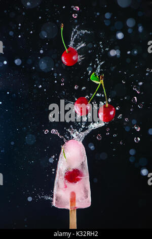 Popsicle with fresh cherries on a dark background, dynamic shot with action, splash, water drops and bokeh. Melting ice cream still life with floating Stock Photo