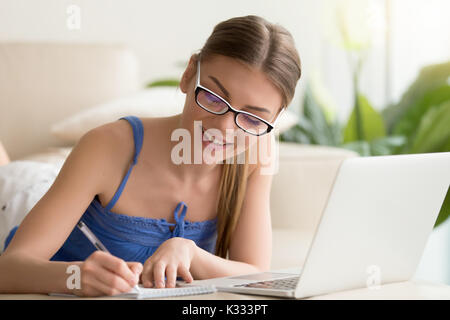 Lady writing in notebook when using laptop at home Stock Photo