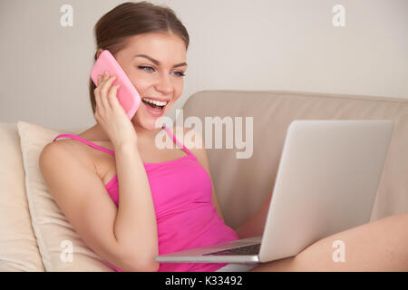 Happy lady talking on cellphone while using laptop Stock Photo